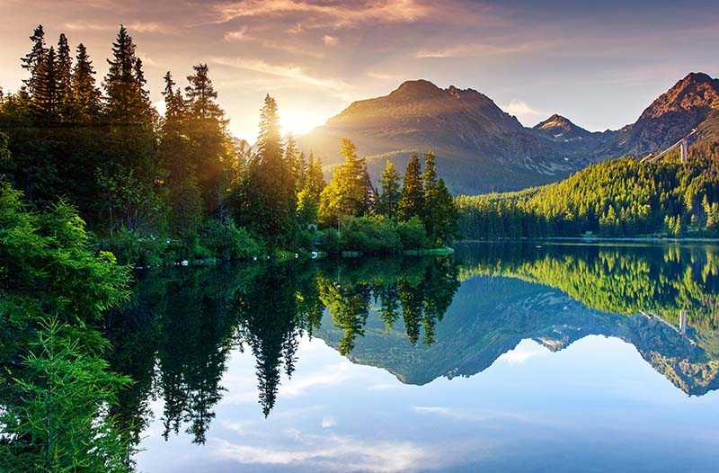 Sun peaking behind mountain with lake